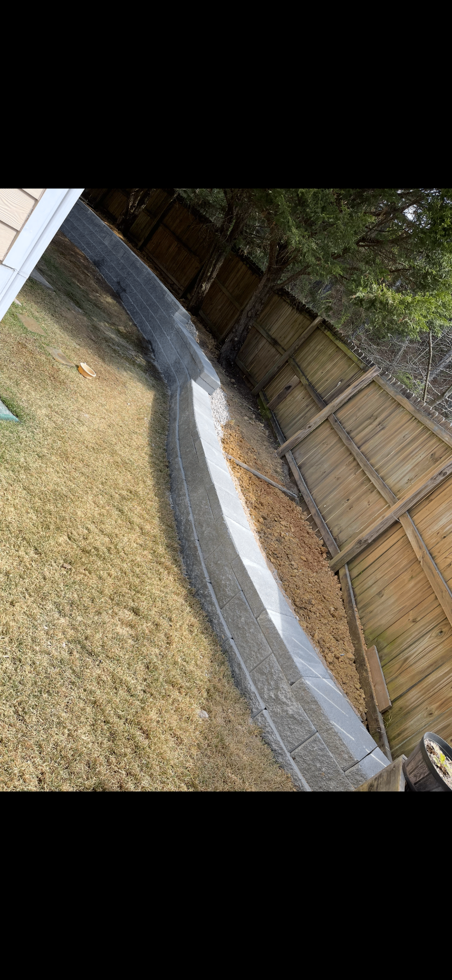 Long curving gray retaining wall following a fence line