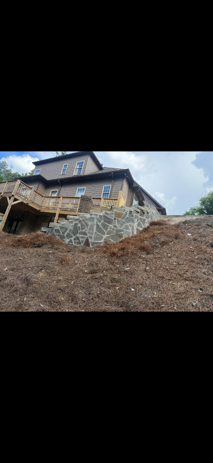 Natural stone retaining wall supporting a large home deck on a steep slope