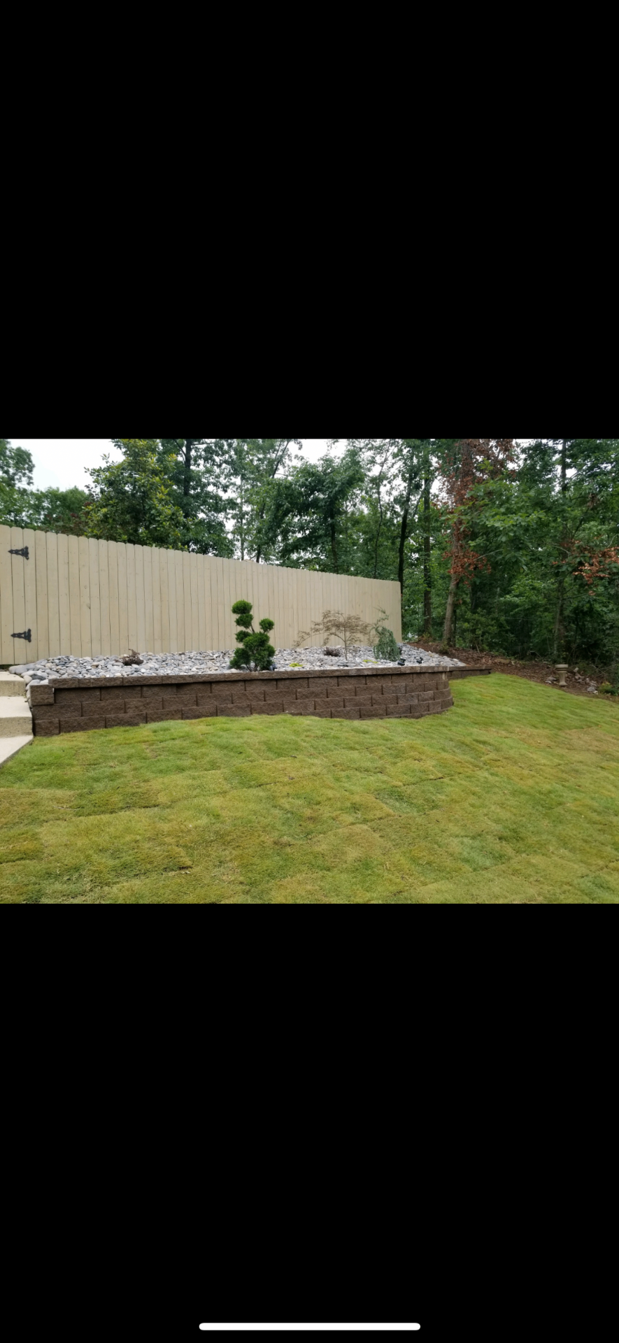 Raised brown block planter-style retaining wall with fresh landscaping and sod