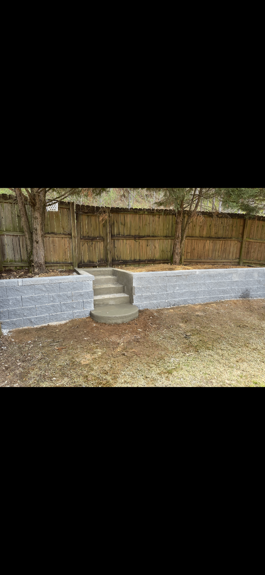 Gray retaining wall with concrete steps along a wooden fence