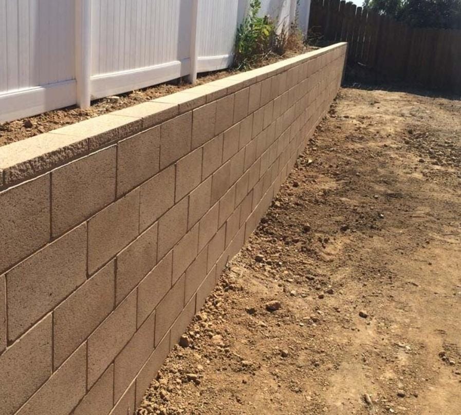 Straight tan retaining wall running along a fence line